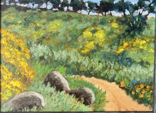 A dirt path winds through a green, hilly landscape with yellow flowers, large rocks, and trees in the background under a blue sky—a scene reminiscent of the tranquil vistas often captured by Ron Zolkover.