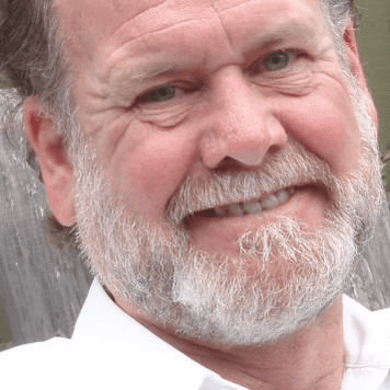 Close-up of Doug Singletary, an older man with a beard, smiling and wearing a white shirt.