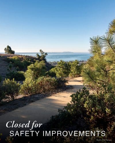 Pathway overlooking the ocean, surrounded by lush trees and bushes, features a Closed for Garden Safety Improvements sign.