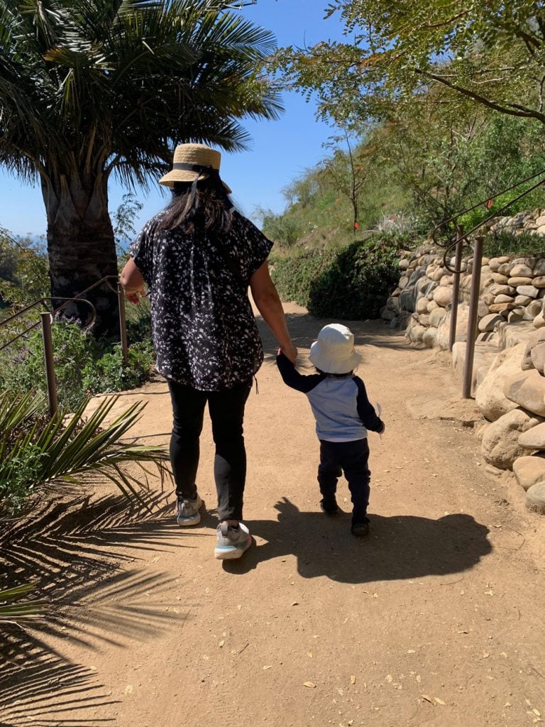A woman and child walking hand in hand on a garden trail at Ventura Botanical Gardens, in bloom cont.